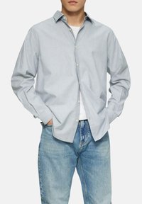 Lichtblauwe overhemd met een subtiel stippenpatroon; lange mouwen, gespreide kraag en een relaxed fit, gecombineerd met vervaagde blauwe jeans.