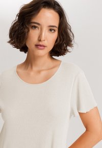 Lysegrå, blød bomulds t-shirt med korte ærmer og rund halsudskæring. Har delikate bølgede kanter på ærmerne.