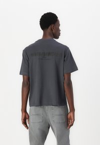 Tricou scurt cu mânecă, de culoare gri închis, cu un logo mare, texturat, pe spate. Fabricat din bumbac moale, cu o croială lejeră.