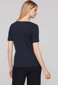 Camiseta negra de manga corta con un escote ligeramente redondeado, fabricada en una tela suave. Textura suave, diseño simple y corte relajado.