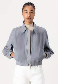 Giacca bomber grigia chiara con zip frontale, polsini e bordo elastici. Materiale morbido con dettagli trapuntati lungo la zip.