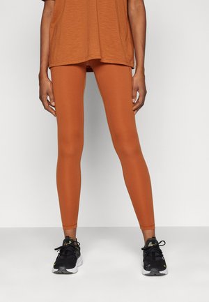 Rustfargede tights laget av glatt, elastisk stoff, tilpasset design, med høy livvidde, parret med svarte treningssko.