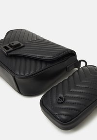 Borsa a tracolla nera trapuntata con chiusura a patta e gancio. Include un piccolo sacchetto abbinato con un motivo a zigzag simile e dettagli del logo.