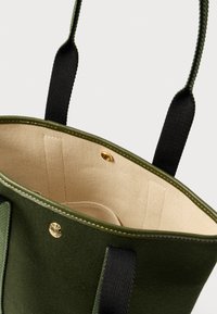 Zelená kabelka z plstěné tkaniny s černými látkovými uchy, s béžovou vnitřní podšívkou, zlatým zapínáním na cvoček a ozdobným prošitím podél horního okraje.