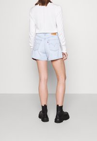 Shorts in denim azzurro chiaro con vita alta, dotati di tasche posteriori e una patch in pelle con logo. Abbinati a una maglietta bianca a maniche lunghe e stivali neri.