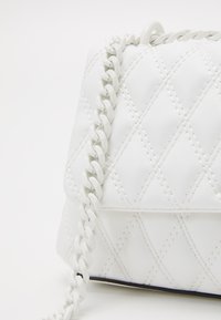 Borsa a mano bianca trapuntata realizzata in materiale sintetico. Dotata di una tracolla a catena intrecciata e un sottile motivo di cucitura. Design compatto e quadrato.
