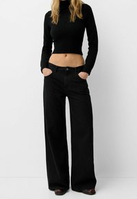 Suéter negro corto con textura de canalé, combinado con pantalones negros de tiro alto y pernera ancha que cuentan con bolsillos y cierre de botón.