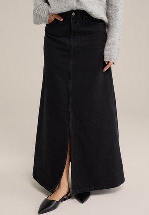 Zwarte denim maxi rok met een voorzijde spleet, hoge taille en subtiele stiksels; gecombineerd met platte, puntige zwarte schoenen.