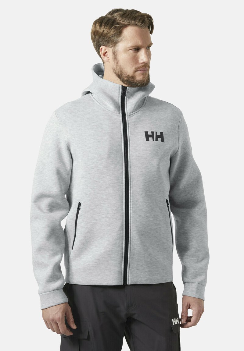 Felpa grigia con zip realizzata in materiale morbido, caratterizzata da un colletto alto, zip nera e logo "HH" sul petto. Texture liscia, senza motivi.