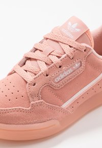 Sneaker in suede rosa chiaro con finitura testurizzata, caratterizzata da un logo bianco, dettagli di design bianchi e perforazioni per la traspirabilità.