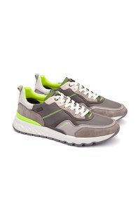 Zapatillas gris y beige con una combinación de cuero y ante, acentos en verde brillante, cordones blancos y una suela de goma texturizada.