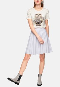 Light beige fitted t-shirt with a sheep graphic, paired with a pleated, light gray skirt and gray ankle boots with black accents.