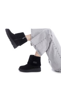 Botas de tobillo negras hechas de material suave, con una parte superior texturizada y suela de goma gruesa. Presentan una cremallera lateral y un acento de logotipo.