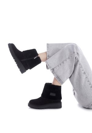 Botas de tobillo negras hechas de material suave, con una parte superior texturizada y suela de goma gruesa. Presentan una cremallera lateral y un acento de logotipo.