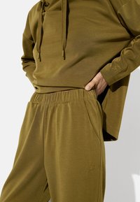 Oliwkowa bluza z kapturem z troczkami i kieszenią kangurką, dobrana do pasujących dresów z elastyczną talią i bocznymi kieszeniami.