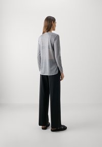 Lichtgrijze lange mouw top met een ontspannen pasvorm, voorzien van een ronde hals en subtiele textuur. Gecombineerd met zwarte wijde broek en sandalen.