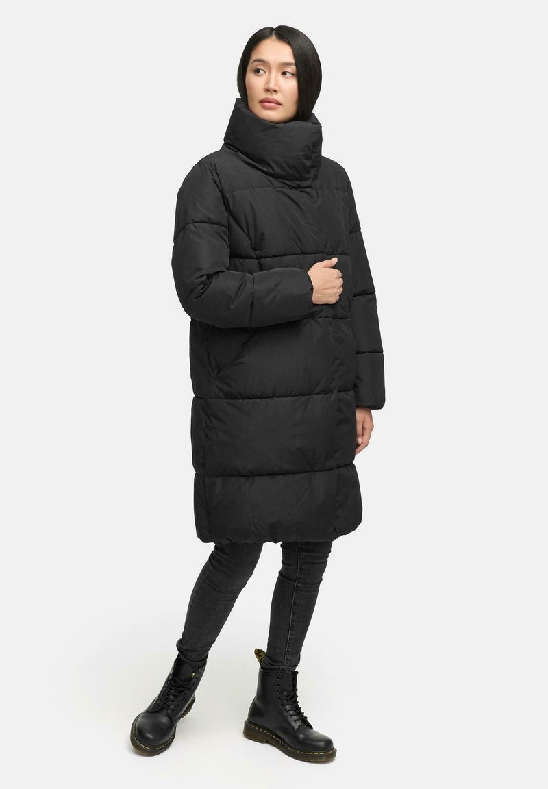 Black puffer coat with high collar, quilted design, and long fit. Worn over black skinny jeans and chunky black boots.