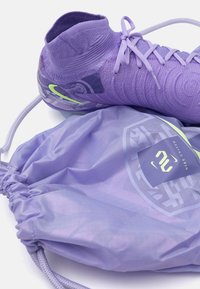 Botas de fútbol moradas con diseño texturizado y acento verde; combinadas con una bolsa de cuerda a juego que presenta un logo y un patrón geométrico.