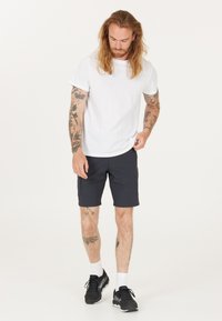 Hvid bomulds t-shirt, marineblå shorts, sorte sportssko og hvide sokker. Synlige tatoveringer på armene. Simpelt, afslappet design.