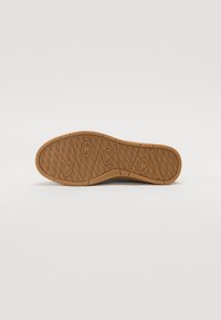 Semelle en caoutchouc avec un motif texturé beige, comportant des rainures et des accents circulaires, conçue pour l'adhérence et la durabilité.