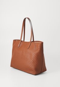Brązowa pleciona skórzana torba tote z dwoma długimi uchwytami, prostokątnym kształtem, teksturowaną powierzchnią i detalami w postaci lamówki wzdłuż górnej krawędzi.