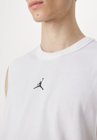 Hvid bomulds ærmeløs t-shirt med en sort silhuetlogo på brystet og en rund hals med ribkant.