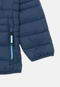 Dunkelblauer Pufferjackenbereich mit gesteppter Textur, ausgestattet mit einem kontrastierenden hellblauen Reißverschluss und einem bündchenförmigen Ärmelabschluss.
