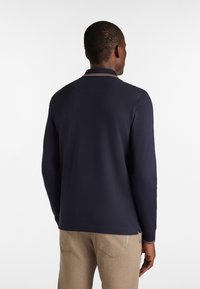 Marineblaues Poloshirt mit langen Ärmeln und kontrastierendem Kragenbesatz, aus einem glatten Baumwollgemisch gefertigt. Bietet eine lockere Passform und keine sichtbaren Grafikdesigns.