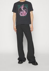 Camiseta gráfica negra con un diseño de serpiente multicolor y el texto "THE KOoples ABOVE ALL RULES", combinada con pantalones de pierna ancha negros y zapatos chunky.