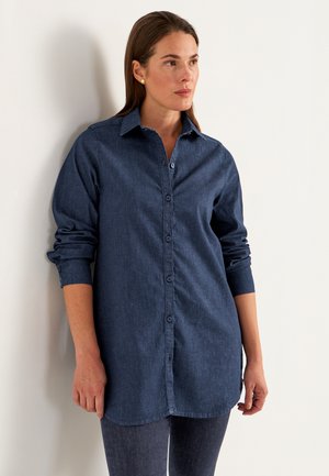 Mörk denimskjorta med knäppning, långa ärmar som är uppvikta vid manschetterna och en rundad nederkant. Slät textur, klassisk kragstil.