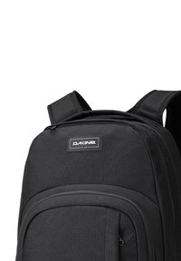 La mochila negra cuenta con un tejido duradero, correas de hombro acolchadas y un bolsillo frontal con cremallera. Incluye un prominente parche con el logo de la marca.