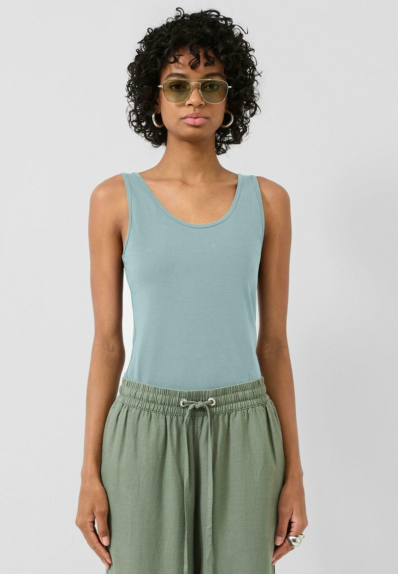 Hellblaues Tanktop mit rundem Ausschnitt, kombiniert mit lockeren grünen Hosen mit elastischem Bund und Kordelzug.