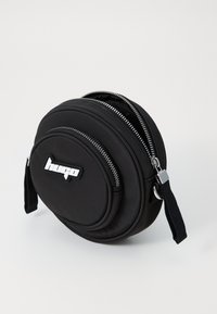 Borsa circolare nera con superficie in tessuto liscio, due cerniere e un'etichetta con logo. Presenta una tracolla removibile e dettagli in hardware argentato.