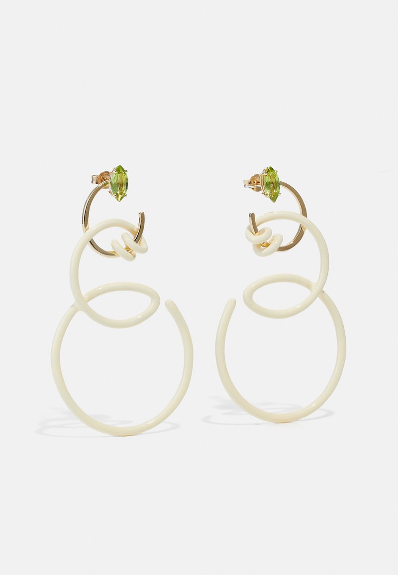 Pendientes color crema que presentan bucles y círculos entrelazados, acentos dorados y vibrantes piedras preciosas verdes en la parte superior.