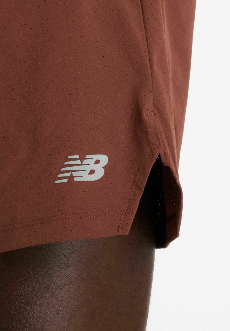 Bruine sportshorts met een geperforeerde textuur. Voorzien van een wit New Balance-logo bij de zoom en zijopeningen voor bewegingsvrijheid.