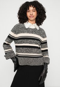 Črno-bela striped pletena pulover z teksturiranim zaključkom, z debelim robom in manšetami, nošen čez srajco s ovratnikom.