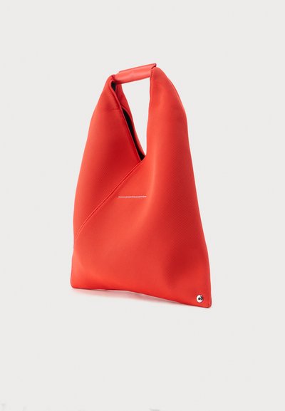 Κόκκινη υφασμάτινη τσάντα tote με τριγωνικό σχήμα, κοντή λαβή και μεταλλική τρύπα στη γωνία του πάτου σε λευκό φόντο.