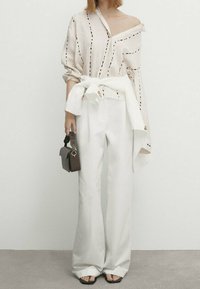 Camicia in misto lino con strisce diagonali, design off-shoulder; pantaloni bianchi a vita alta; piccola borsa marrone; scarpe nere open-toe.
