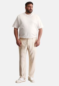 Beige katoenen broeken met een relaxte pasvorm, twee zijzakken, lichte textuur, gecombineerd met een eenvoudige witte T-shirt met korte mouwen en witte sneakers.