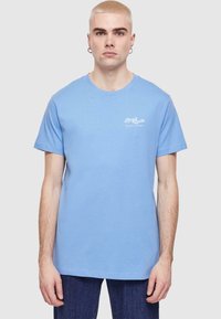 Šviesiai mėlynas medvilninis marškinėliai su apvaliu iškirpimu ir trumpomis rankovėmis. Ant kairiojo krūtinės puikuojasi baltas spausdintas logotipas. Sukurta su mėlynais džinsais.