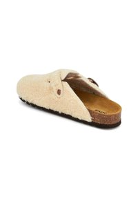 Fuzzy cream slipper with a cork sole, rounded shape, and two dark buttons. Soft texture with an open-back design for easy wear.