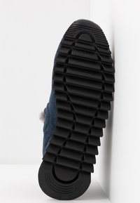 Chausson en suede bleu marine avec une surface texturée, doté d'une semelle en caoutchouc noire avec de profonds rainures pour une meilleure traction et d'un accent en fourrure sur le côté.