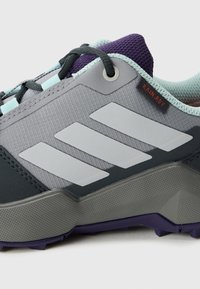 Close-up of gray and purple hiking shoe with black laces, light blue trim, textured sole, and "RAIN.RDY" tag near ankle collar.