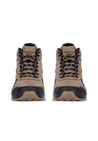 Beżowe buty trekkingowe z czarnymi akcentami, z wyściółką w kołnierzu, grubymi czarnymi sznurowadłami i wytrzymałymi podeszwami zapewniającymi przyczepność. Widoczne logo Reebok.