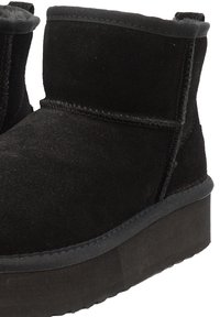 Black suede ankle boots with a rounded toe, stitched seams, and a textured rubber sole. They have a flat platform design.