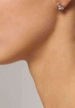 Gros plan sur le cou et la mâchoire d'une personne portant une boucle d'oreille clou en argent ornée d'une gemme claire et facettée.