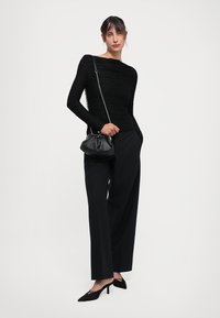 Black long-sleeve top with textured pleats, paired with loose black trousers and sleek black heels. A small black bag with a silver chain strap.