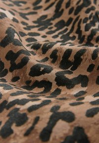 Tissu à imprimé léopard présentant un fond beige texturé avec de gros points noirs, mettant en valeur un matériau tissé dans une apparence douce et drapée.
