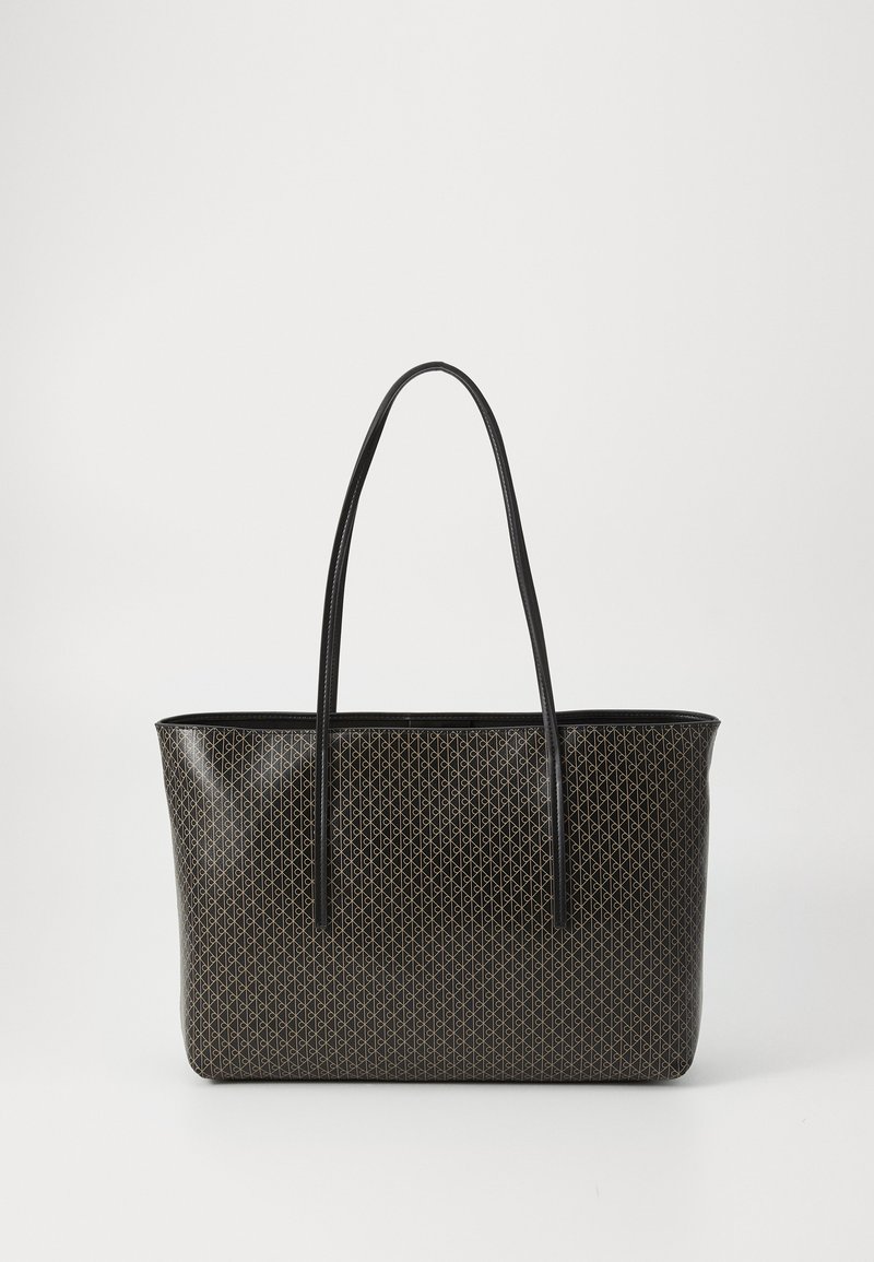 Sac fourre-tout noir avec de longues poignées et un motif géométrique beige répétitif sur une surface lisse, sur fond uni clair.