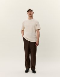 Beige rövid ujjú ing, barna bő szárú nadrág, fekete cipő és világosbarna sapka sötét akcentusokkal. Simáb szövet és laza szabás.